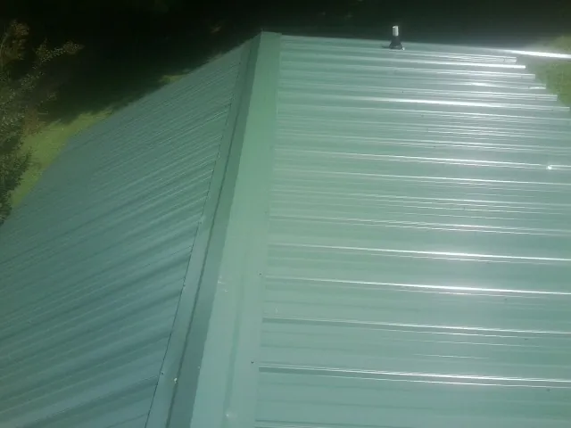 New green metal panels meeting at the ridge of a roof — Flat Roof Repair work by our crew in Sherwood