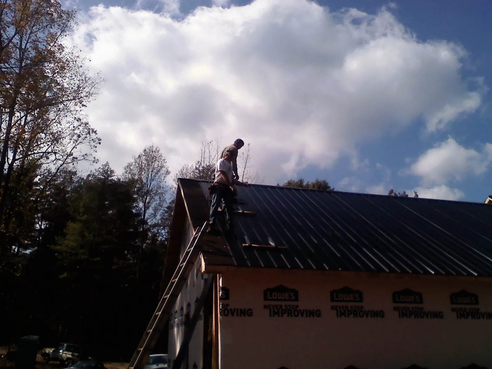 Roofer fastening dark metal panels high against a cloudy sky, from a Roof Inspection job in Sherwood